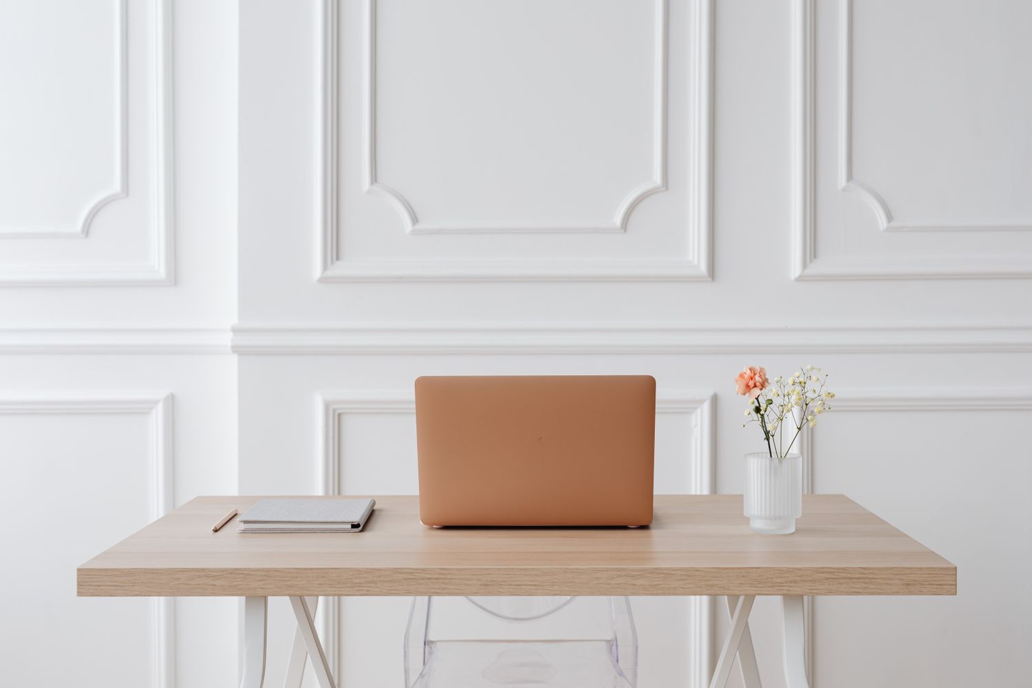 A simple desk with a laptop and flowers before a white wall.